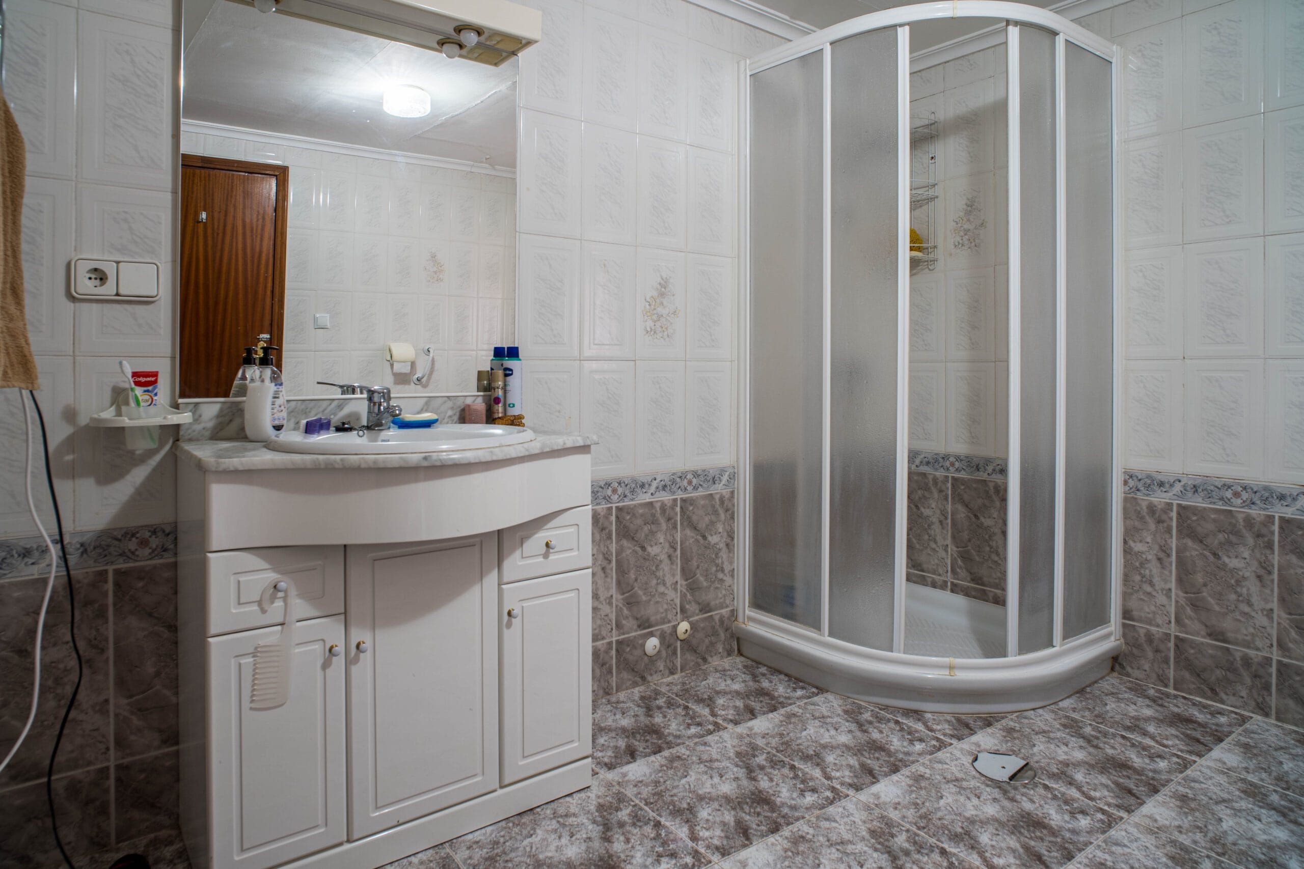 Bathroom with a corner shower cabin with frosted glass doors, a white vanity with a sink and mirror, and tiled walls and floors.