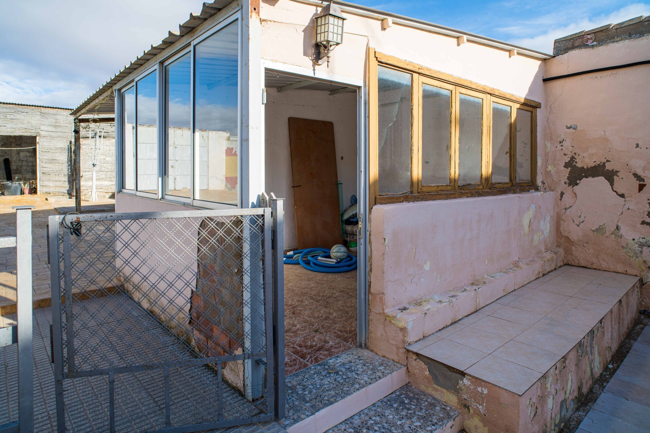 Outdoor patio with tiled steps leading to a small enclosed storage room with glass windows and a metal gate in front.