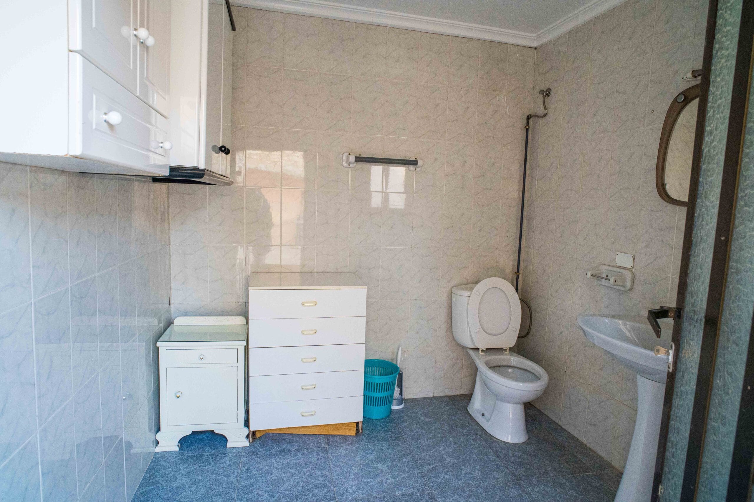 Bathroom interior showing a toilet with the seat up, a white sink, white storage cabinets, and tiled walls and floor.